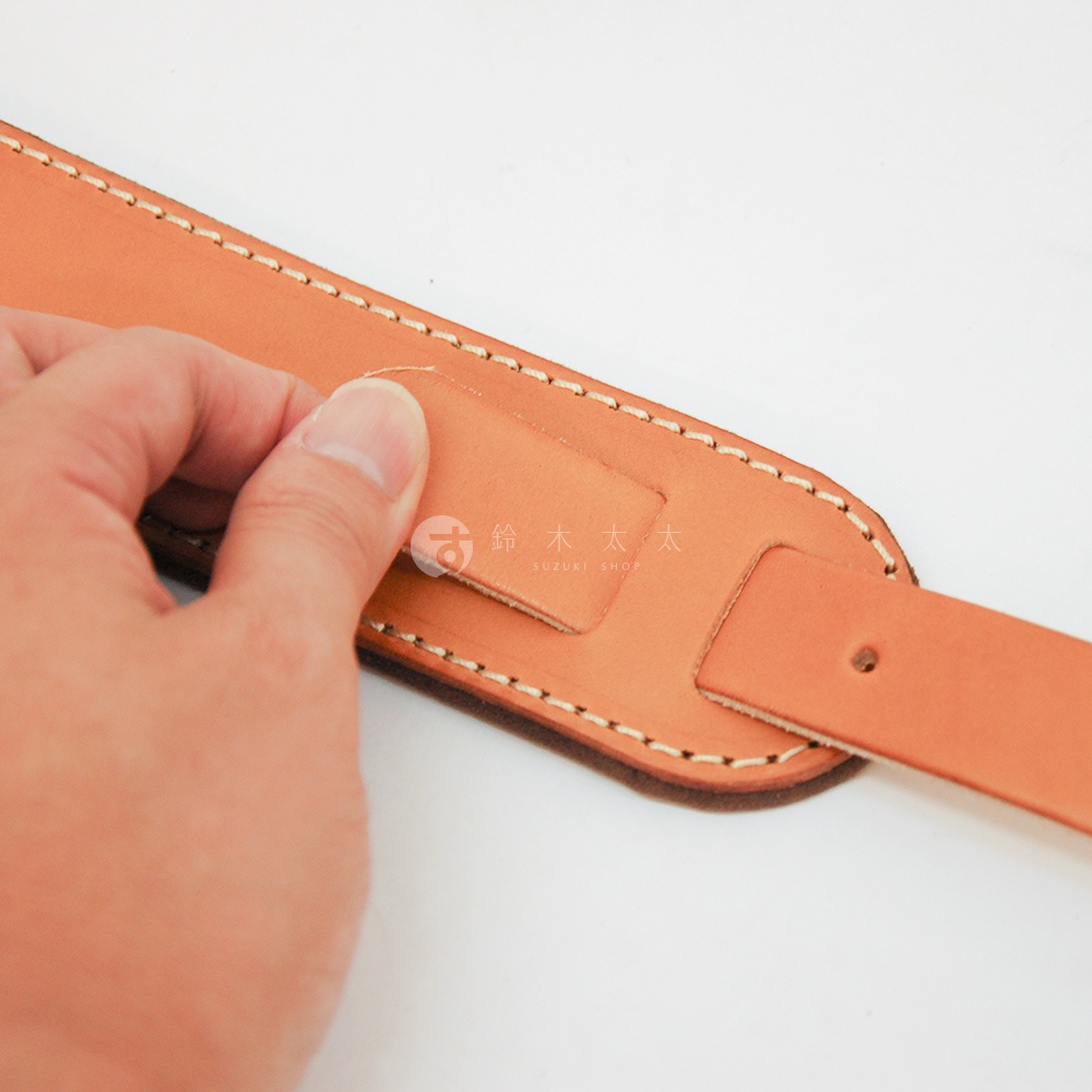 職人手作淺棕色皮革Big肩墊，縫線清晰，局部有扣帶設計，由手部特寫展示產品細節。
