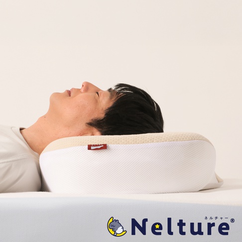 一位男子仰臥在 NELUD 完美釋壓Q彈棉花糖枕上，枕頭呈現米白色網狀外層與淺黃色頂部，側邊有紅色品牌標籤。