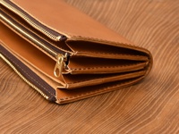 職人手作皮革Organ雙拉鍊L型長夾，採用棕褐色皮革材質，設有兩個金色拉鍊，內部隔層清晰可見，展現皮革自然的紋理與精緻的縫線工藝，置於木紋背景上。