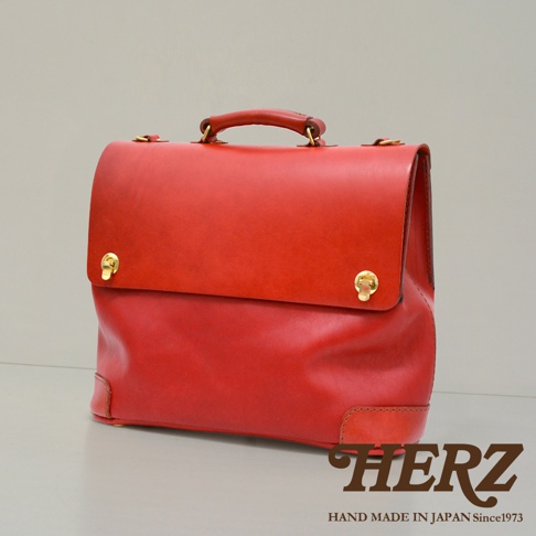 紅色皮革製成的波士頓包，頂部有提把，正面有金色旋轉鎖扣，包包底部有加固的皮革飾片。