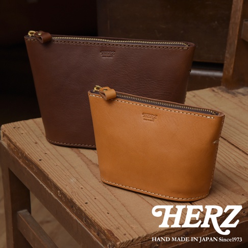 兩個職人手作皮革三角收納包，一個為深棕色，另一個為淺棕色。兩者皆為皮革材質，配有金色拉鍊。