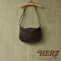 職人手作皮革Organ單肩半月包，深棕色，光滑皮革材質，半月形輪廓，單肩背帶，拉鍊開合，掛於木質衣架上。