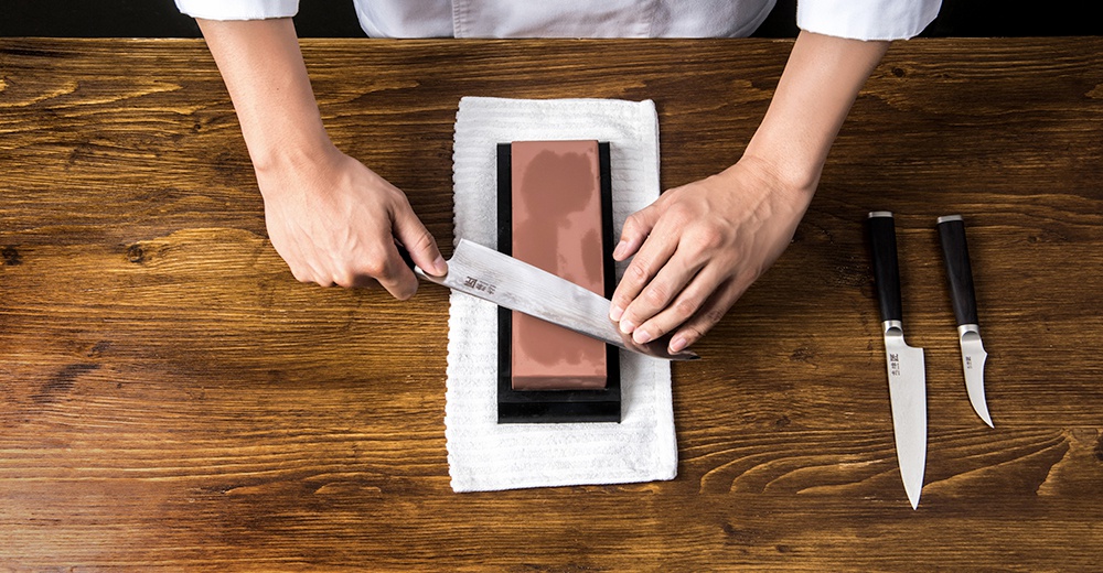 廚師用磨刀石磨利刀刃，旁邊擺放兩把刀