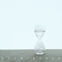 awaglass 泡時計，由透明玻璃製成，整體呈現沙漏形狀。上方球狀玻璃瓶裝有少量透明液體，並帶有細小的氣泡。下方球狀玻璃瓶也充滿了細緻的氣泡。產品置於灰色紋理的平面上，背景為淺色。