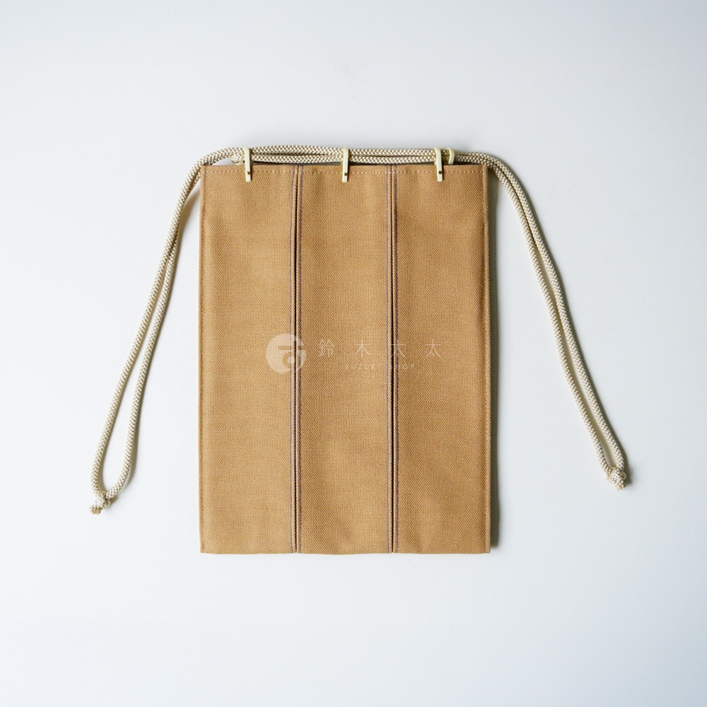 這是一款京都KOSHO品牌的ougi帆布信玄袋，呈現極簡的米棕色調。包身採用耐用的厚帆布材質，設計簡約俐落，配有三條直向縫線裝飾。頂部設有白色繩結穿孔，搭配米白色粗繩抽繩設計，整體外觀清新雅緻，充滿日式手工藝的質感。