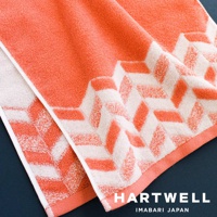 一條珊瑚橘色與白色交織的今治浴巾，以傳統幾何圖紋織成，觸感細緻，適合日常使用。