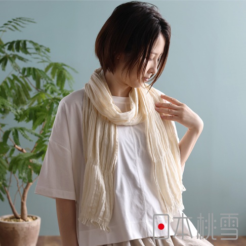 一位留著短髮的女性模特兒，身穿白色寬鬆棉質上衣，脖子上圍著一條米白色、帶有細緻直條紋理的輕薄紗布圍巾，圍巾末端有流蘇裝飾。背景為簡約的淺藍綠色牆面與一盆綠色植物，畫面右下角帶有日本桃雪的品牌標誌。