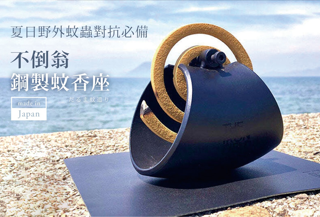 黑色鋼製不倒翁蚊香座，帶有兩個金黃色環，置於海邊的沙灘上。