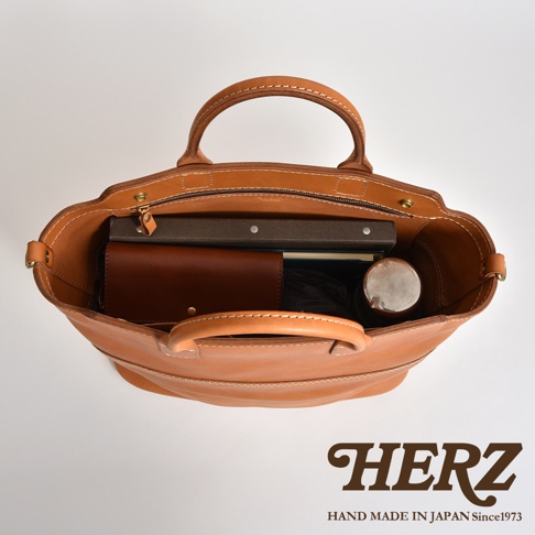 職人手作皮革托特包，淺棕色，頂部視角，包內裝有書本、皮夾和保溫瓶。