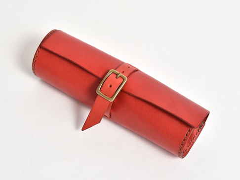 紅色皮革捲捲筆袋，附有金色皮帶扣，用於固定，邊緣有縫線。