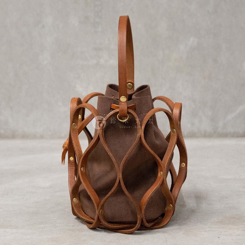 日本HERZ職人手作皮革Organ編織水桶包，深棕色麂皮內袋搭配焦糖色皮革編織外框，提把為焦糖色皮革，包身上有品牌標誌，整體為垂直視角拍攝。