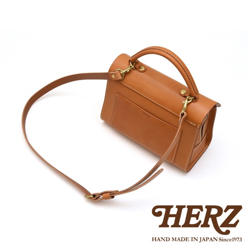 日本HERZ手工製作的駝色牛皮多功能收納單肩包，附可拆卸背帶，可手提、肩背或斜背，包身有HERZ壓印商標。