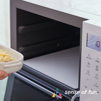 白色微波爐內部，放置一個盛有起司食物的白色陶瓷碗，微波爐門半開，內部有淺灰色防污保護墊。