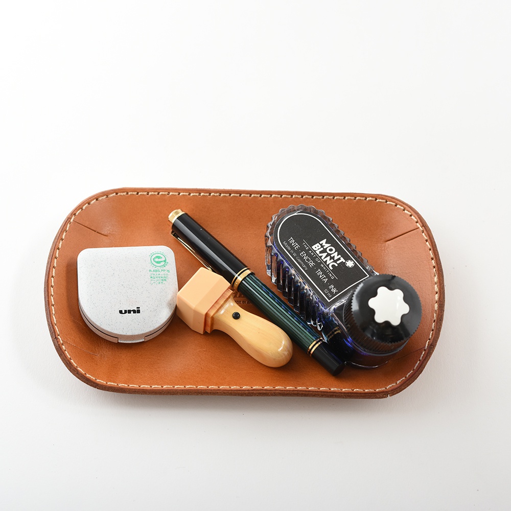 職人手作皮革小物收納盤，棕色皮革，盤內放置一支綠色條紋鋼筆、一瓶Montblanc墨水和一個白色的小盒子。