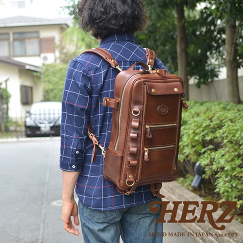 職人手作皮革兩用多功能後背包 R-66，採用深棕色皮革材質，設計有頂部提把、側邊掛環、拉鍊主袋及多個前置拉鍊口袋，金屬五金配件為黃銅色。