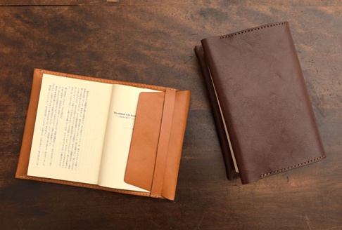深棕色皮革翻蓋記事本書套，內含一本打開的書，書本內頁為淺黃色，書套內部有相同顏色的皮革置物夾。
