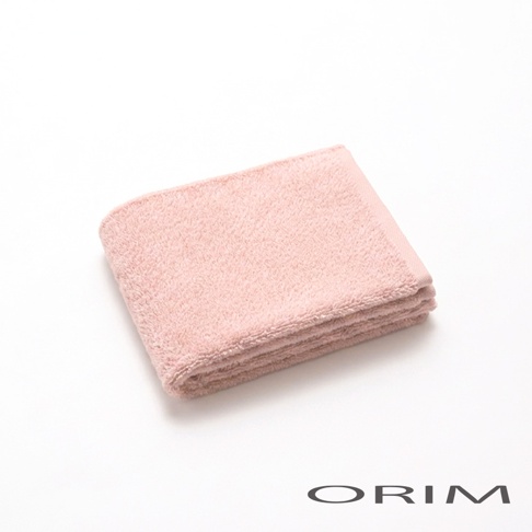 一張放置於白色背景上的淡粉色 ORIM 今治輕羽恆柔耐久毛巾，毛巾表面呈現蓬鬆柔軟的棉質紋理，呈現長方形摺疊狀，右下角印有黑色的 ORIM 品牌標誌。