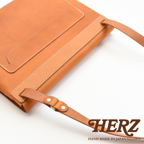 職人手作皮革經典郵差包 CK-4 S，採用溫暖的棕褐色皮革製成，表面飾有精緻的縫線及品牌壓紋，搭配可調節的皮革背帶與金屬扣環，展現簡約經典的設計風格。