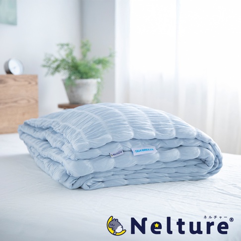 Nelture 涼爽夏夜舒眠單人被，淺藍色，表面有細緻的紋理，觸感柔軟，在床上呈現蓬鬆的摺疊狀態，左側有 Nelture 品牌標籤，右側有 SEA BREEZE 標籤。