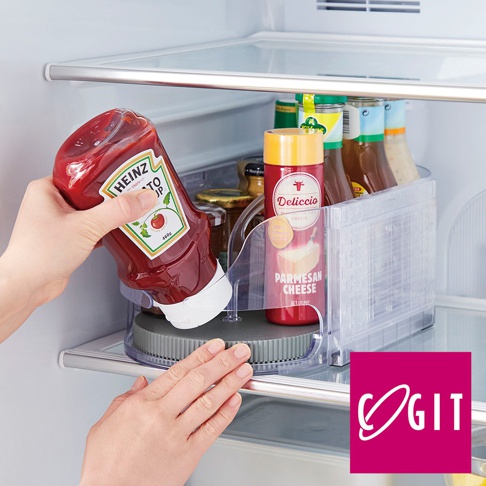 透明壓克力製成的多功能橢圓旋轉調味收納盤，盤內裝有數瓶醬料，其中一瓶番茄醬正被手拿起，盤的底部為灰色旋轉底座。