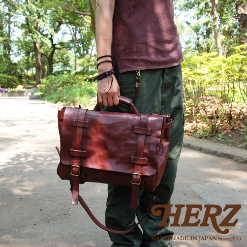 職人手作復古風皮革郵差包，深棕色，附有雙皮帶扣和提把，展現自然紋理與質感。