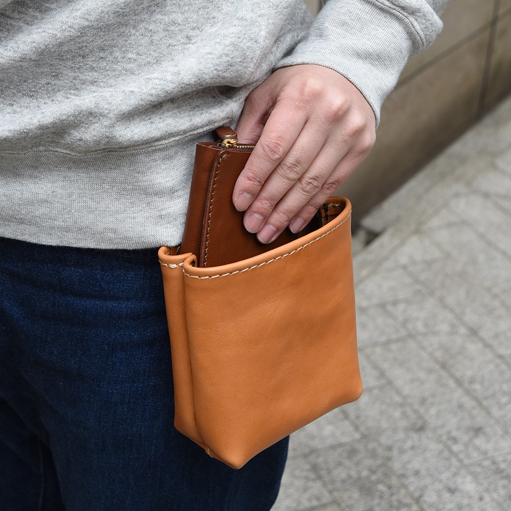 棕色皮革腰袋，配有明顯的米白色車線，可容納一個棕色皮夾，由一位女士的手插入。