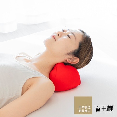 女性仰躺，頭部下方墊著紅色心形指壓按摩枕，枕頭為柔軟布料材質，用於支撐頸部。