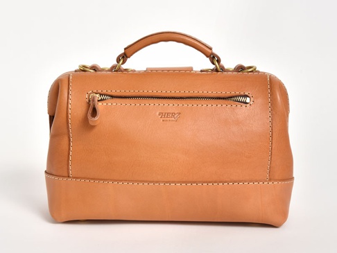 職人手作皮革兩用迷你口金單肩包，採用自然色調的皮革製成，設計簡約。包包正面有一個拉鍊口袋，頂部有提把和金屬環，整體風格經典。
