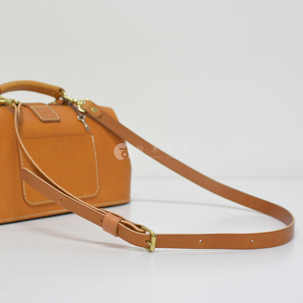 職人手作皮革長型迷你醫生包，採用鞣製皮革製成，呈現溫潤的焦糖棕色。包款配有可拆卸的長肩帶，方便手提或斜挎。細節處可見車縫線和金屬釦環，展現精緻工藝。