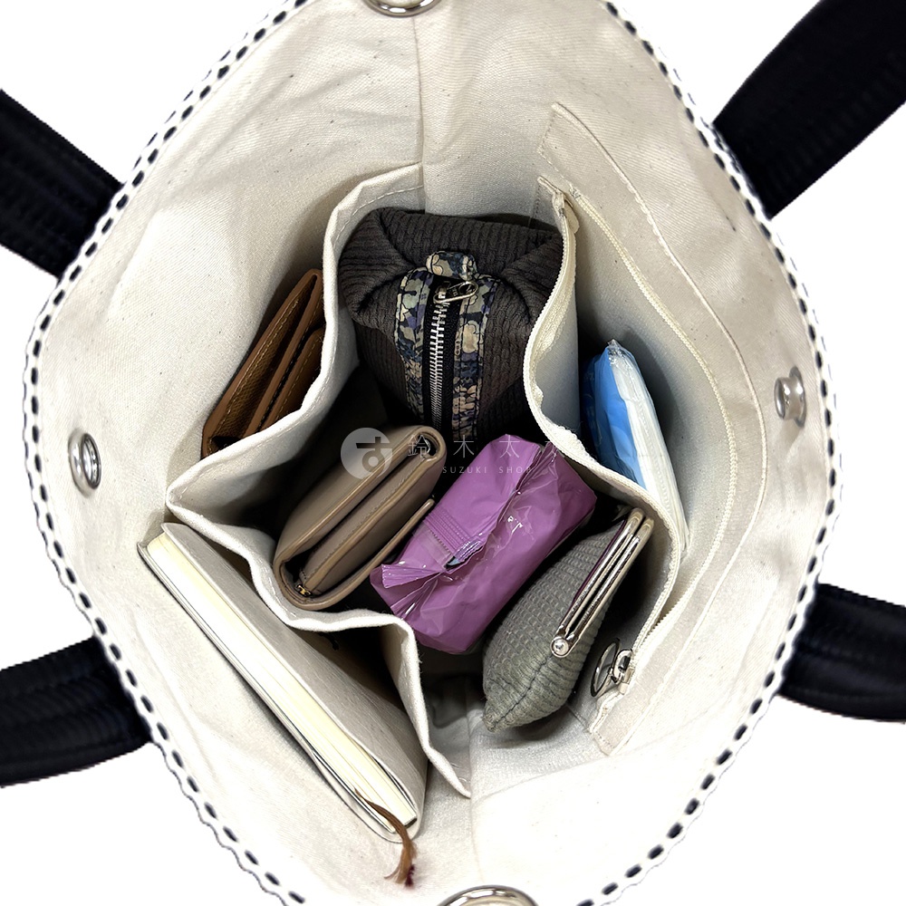 三河木綿刺子織兩用水桶包內部，展示多個隔層，裝有錢包、筆記本、化妝包、濕紙巾及其他小物。包身為米白色，搭配黑色提把，邊緣有黑色繡線裝飾。