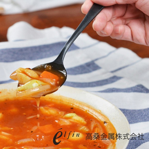 日製熔岩黑石餐匙，由金屬製成，呈現啞光黑色。餐匙盛有燉煮的蔬菜料，如胡蘿蔔、洋蔥和綠色蔬菜，浸在紅色的湯汁中。