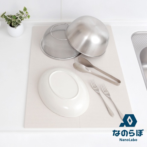 NANOLABO 品牌 logo 旁顯示日文「なのらぼ」及英文「NanoLabo」，圖片為廚房一景，展示一個橢圓形白色盤子，兩個不鏽鋼夾子，兩個叉子，一個不鏽鋼濾網盆，以及一個不鏽鋼碗，皆放置於淺米色波浪紋的吸水墊上。