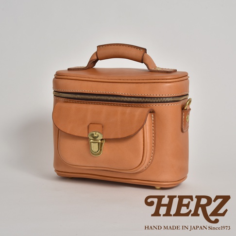 職人手作皮革相機包，經典棕色，柔軟皮革材質，圓潤造型，頂部設有提把及拉鍊，前方有一個翻蓋式口袋，並以金屬釦固定。