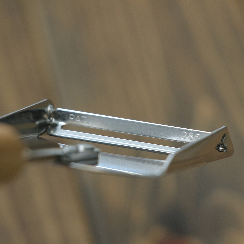 VEGET 不鏽鋼木柄削皮刀，刀片為銀色不鏽鋼材質，印有「PAT」和「285」字樣。削皮刀的刀刃部分呈現平行雙軌設計，刀頭部分為彎曲的銀色不鏽鋼。