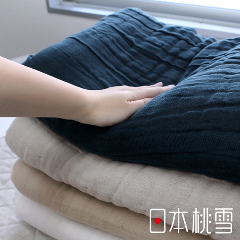 深藍色、淺米色和白色八層紗雙人被堆疊。左側有一隻手輕撫在最上層的深藍色被子上，展示其柔軟紋理。