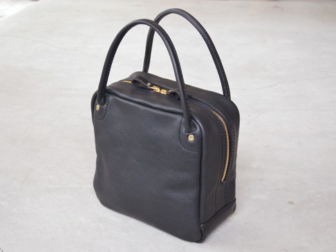 黑色皮革方形托特包，配有金色拉鍊和皮革手柄。