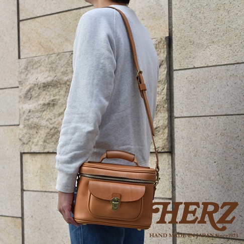 職人手作皮革軟皮相機包，採用經典棕色皮革，帶有頂部提把、可拆卸肩帶、拉鍊主隔層及前方翻蓋口袋，口袋上飾有復古金屬鎖扣。