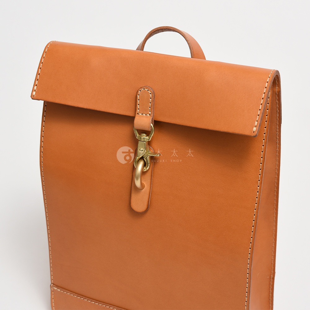 職人手作皮革紙袋風後背包，採用光滑皮革材質，顏色為淺棕色，配有金色金屬扣環及提把，縫線清晰。