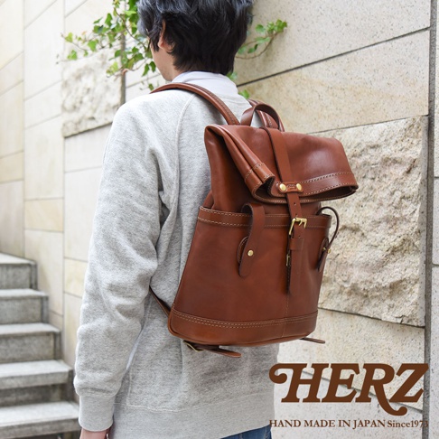 職人手作皮革雙口袋折蓋後背包，採用經典棕色皮革，設有雙前袋、折疊式袋蓋及金屬扣環，展現復古質感。