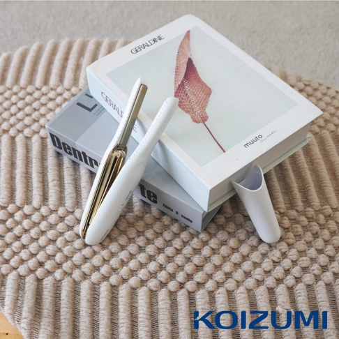 珍珠離子夾 KHS-G650 放置於書本和地毯上，整體為白色帶有金色點綴，造型簡約。