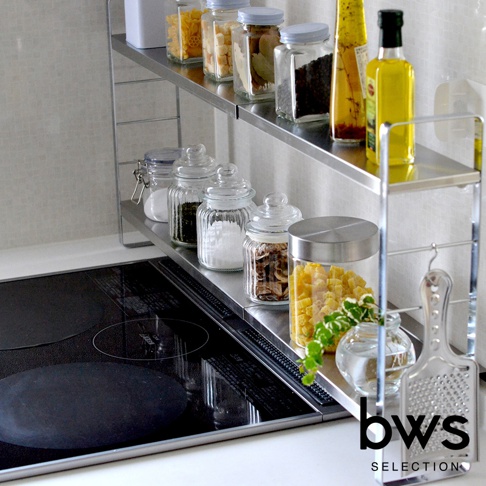 bws SELECTION 伸縮雙層不鏽鋼廚房收納架，架上擺放多種玻璃罐裝食材、調味料及油瓶，爐灶旁的架子上還有刨絲器。
