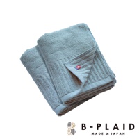 兩條淺藍色直紋毛巾疊放，質地蓬鬆，其中一條毛巾一角有紅色與藍色條紋的品牌標籤。