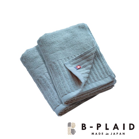 兩條淺藍色直紋毛巾疊放，質地蓬鬆，其中一條毛巾一角有紅色與藍色條紋的品牌標籤。