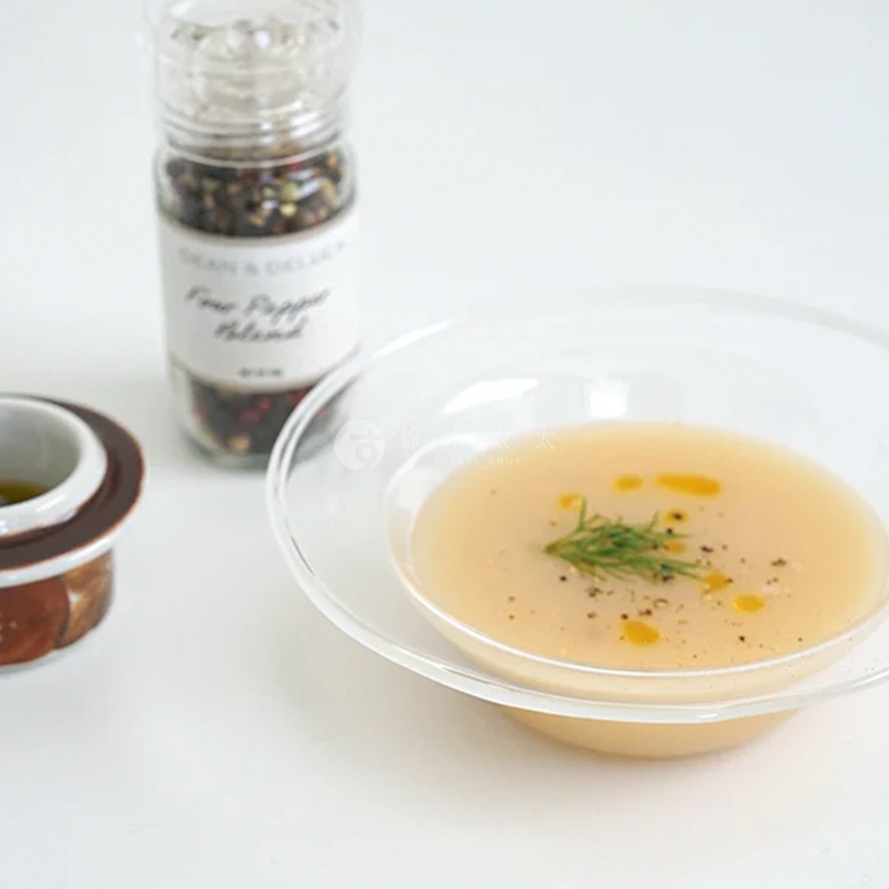 清透玻璃深型點心碗，盛有淺黃色湯品，碗中點綴著香料與油滴，旁有胡椒研磨器與醬料碟。