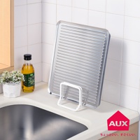 銀色金屬材質的方形瀝水籃，帶有橫向凹槽，置於白色支架上，旁邊有橄欖油瓶和一盆白色小花。