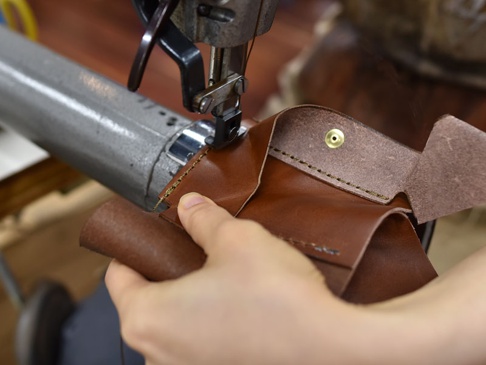 手工縫製的棕色皮革三折式迷你短夾，細節處有黃銅按鈕，展示製作過程。