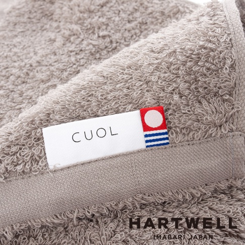 CUOL 品牌標籤縫在淺灰色的細緻毛巾上，毛巾材質柔軟，紋理清晰。標籤一側有紅、白、藍色塊圖案，另一側印有「CUOL」字樣。