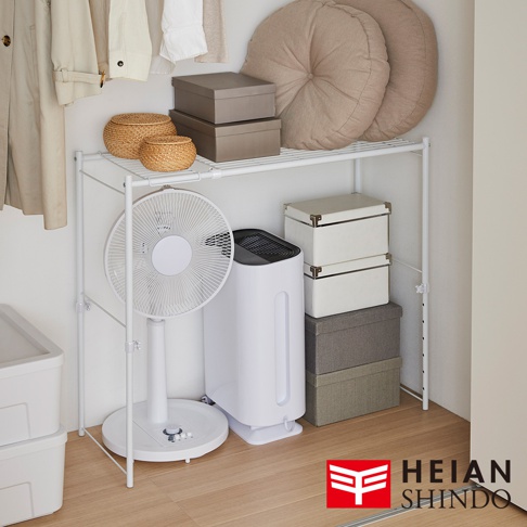 白色兩層置物架，上方擺放兩個藤編收納籃、兩個灰色紙盒及兩個圓形布藝靠墊。下方層架有白色立扇、白色空氣清淨機及疊放的白色、灰色、米色收納盒。