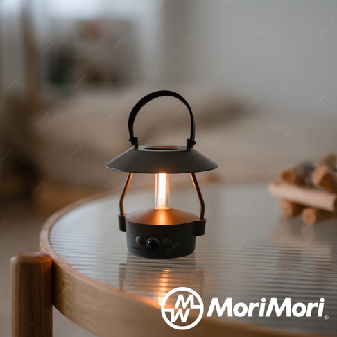 黑色復古風格 LED 燈籠，帶有暖黃色光源，頂部有黑色提把，底部有開關按鈕，放置於透明玻璃桌面。