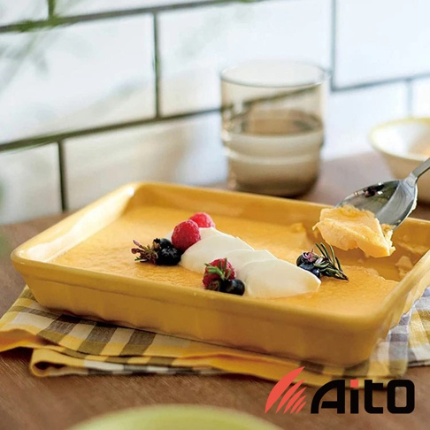 黃色釉彩美濃燒長方烤盤，盛裝著香濃的烤布蕾，上面點綴著鮮紅的覆盆子、藍莓和鮮奶油，一旁有湯匙正在舀起一塊烤布蕾。